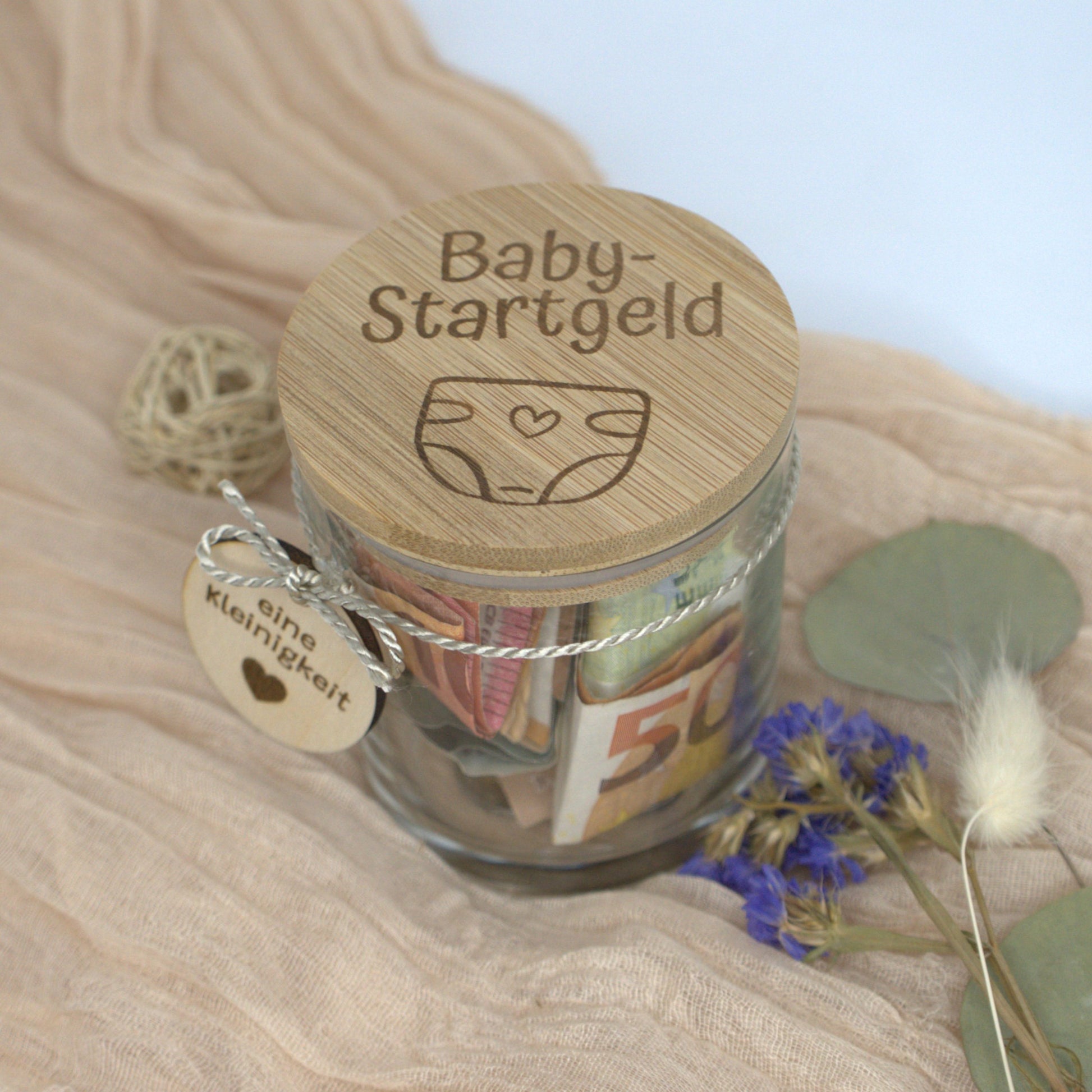 aby-Startgeld Sparglas mit graviertem Bambusdeckel und Geldfüllung auf dekorativer Unterlage