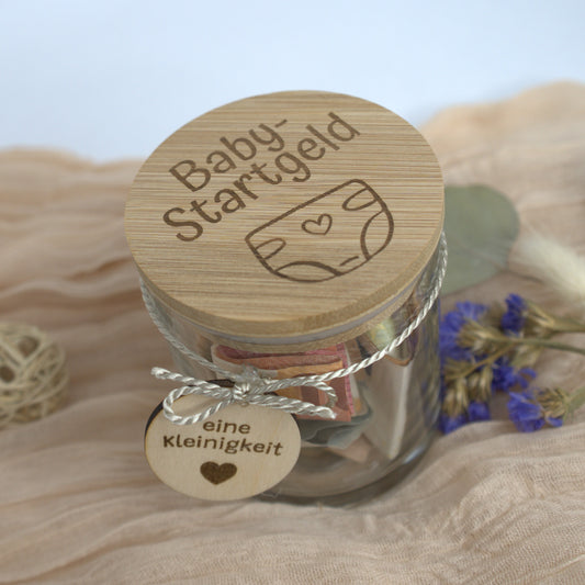Baby-Startgeld Sparglas mit graviertem Bambusdeckel und Geldfüllung auf dekorativer Unterlage