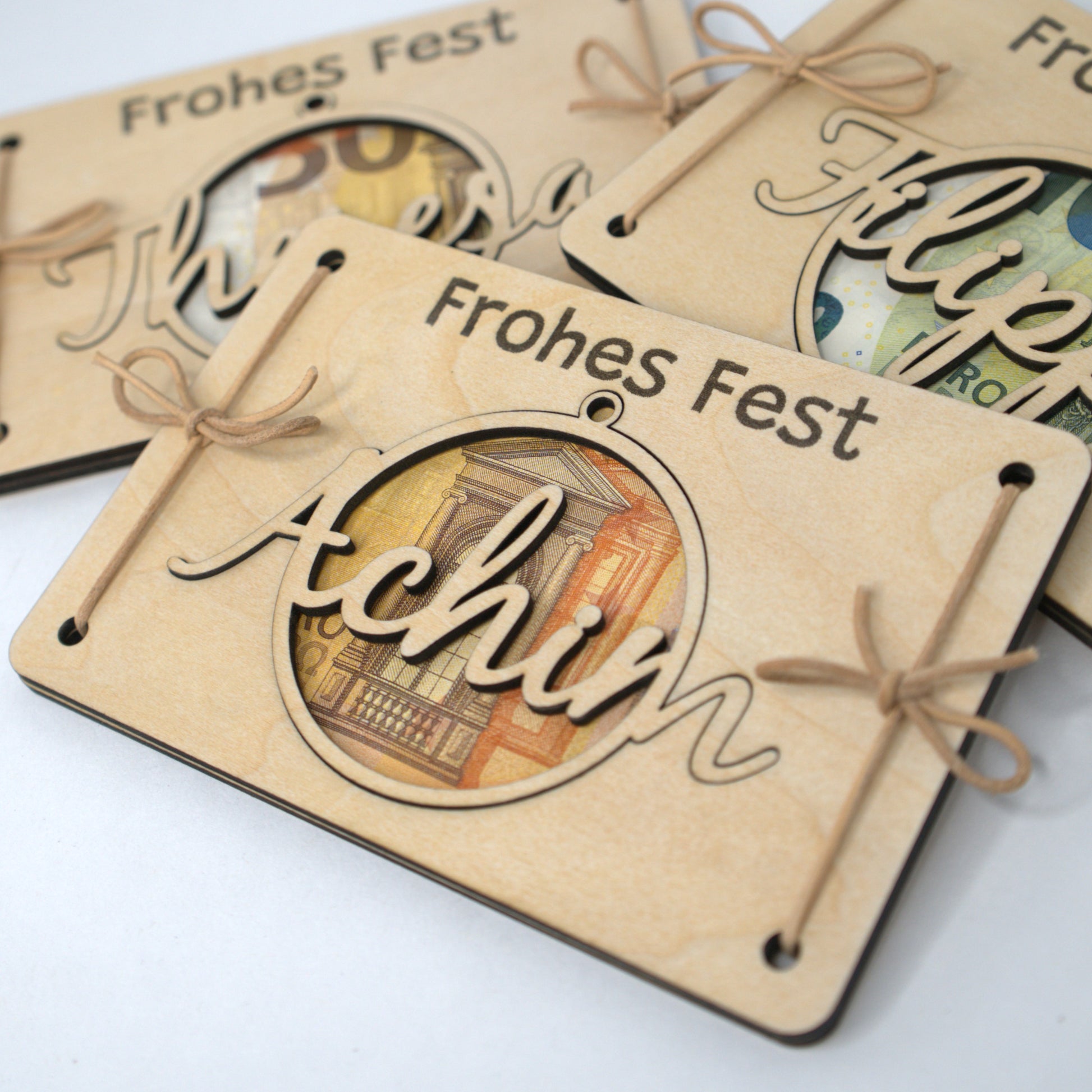 Geldgeschenk Holzkarte Frohes Fest – Namenskugel Achim mit gefalteten Geldscheinen als Weihnachtsgeschenk.